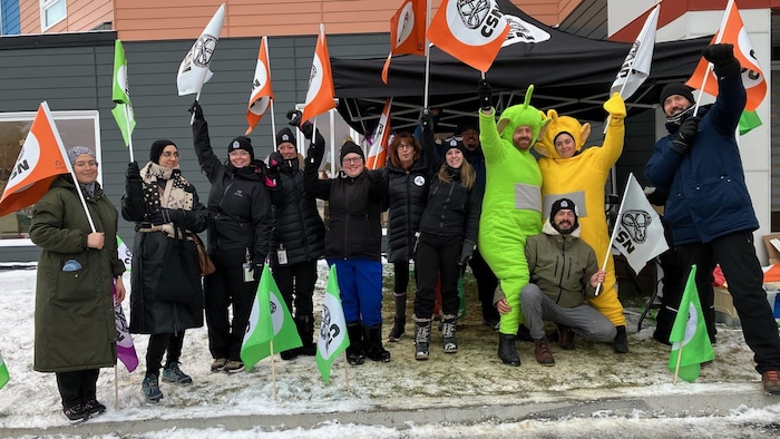 Des employés, dont certains déguisés, manifestent avec des drapeaux aux couleurs de leur syndicat devant le CHSLD.