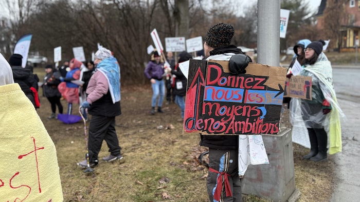 Une personne tient une affiche sur laquelle on peut lire « donnez nous les moyens de nos ambitions ».