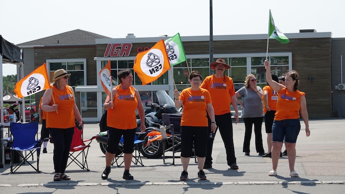 Des employés manifestent avec des pancartes de la CSN devant l'épicerie IGA.