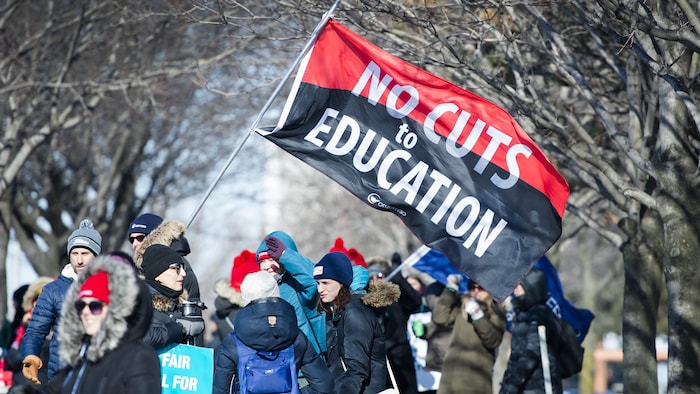 Des enseignants en grève tiennent un drapeau géant qui dit : « pas de coupes en éducation ».