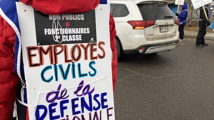 Un employé en grève porte une pancarte sur son dos.