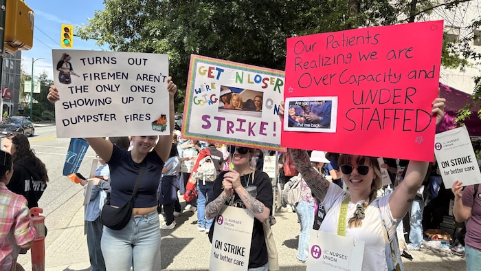 Des femmes tiennent des affiches qui dénoncent les conditions de travail des infirmières.