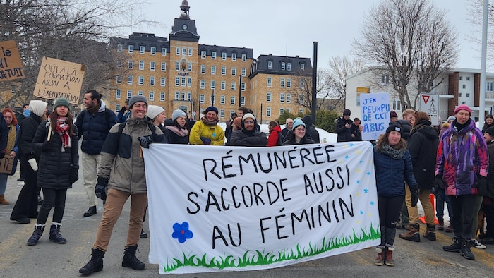 Des dizaines d'étudiants tiennent une grande banderole sur laquelle est inscrit : "Rémunérée s'accorde aussi au féminin".