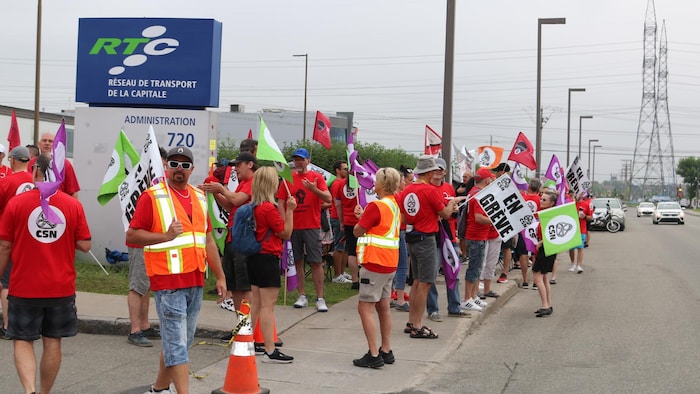 Des chauffeurs en grève du R T C brandissent des bannières aux couleurs de la C S N lors d’une manifestation à l’été 2024.
