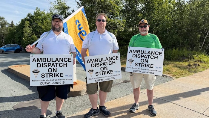 Trois hommes, chacun avec une pancarte qui dit répartiteur d'ambulance en grève. L'un porte un drapeau du syndicat.