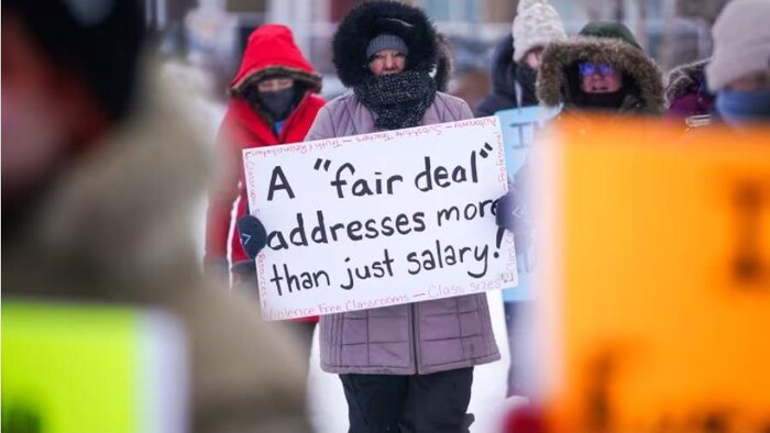 Une manifestante, l'hiver, brandit une pancarte sur lequel annonçant qu'une négociation juste est plus importante qu'un salaire. 