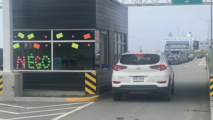 Une voiture est arrêtée à un poste de péage où plusieurs autocollants forment l'abréviation « négo ».