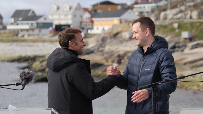 Souriant, Emmanuel Macron serre la main du premier ministre groenlandais, Jens-Frederik Nielsen, dehors, à Nuuk.
