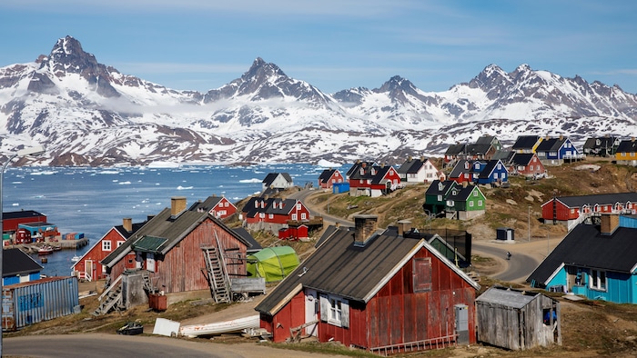 De petites maisons multicolores sont dispersées dans une baie avec en toile de fond des montagnes enneigées. 