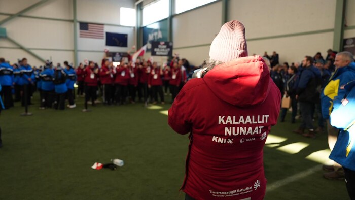 Une athlète du Groenland est tournée de dos et prend une photo de sa délégation, à Mat-Su, en Alaska. 