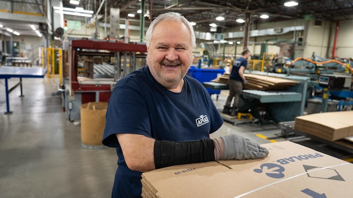 Un homme tout sourire avec la main sur des boîtes.