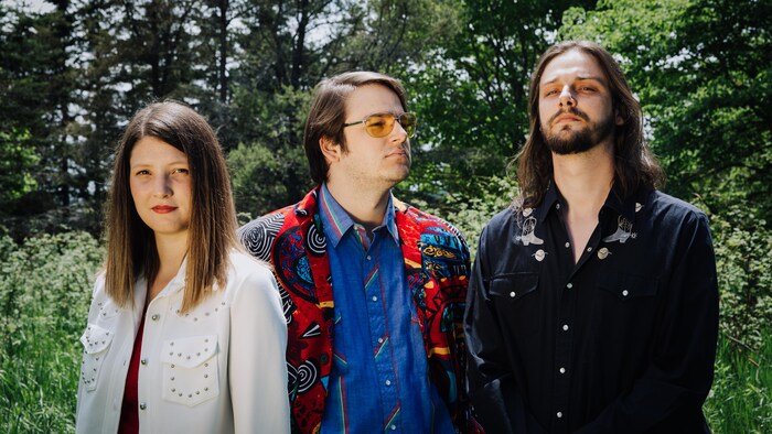Une femme et deux hommes posant pour la caméra devant une forêt.