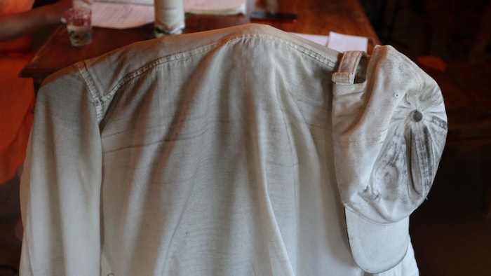 Une chemise et une casquette sales accrochées sur le dossier d’une chaise de cuisine.