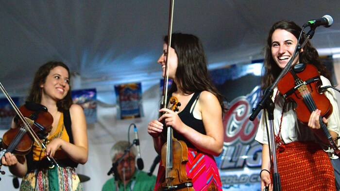 Trois jeunes femmes violonistes sur une scène.