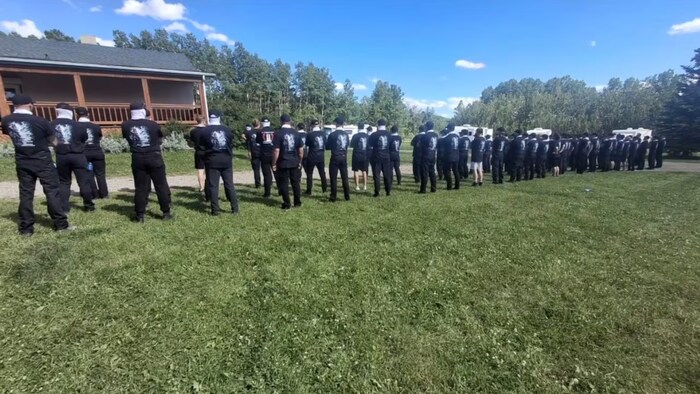 Des hommes cagoulés se tiennent en rangée devant une maison.
