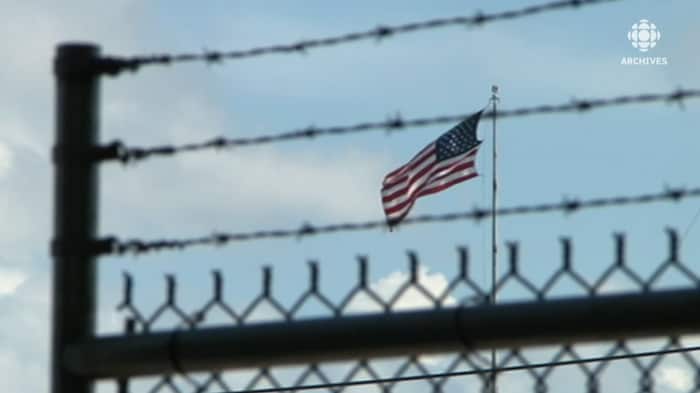 Drapeau des États-Unis qui flotte au vent et clôture de barbelés en avant-plan. 