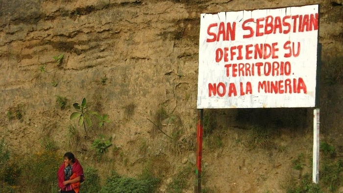 Une femme devant un panneau exprimant son opposition à l'exploitation minière à ciel ouvert. Le panneau dit "San Sebastian défend son territoire. Non à l'exploitation minière".