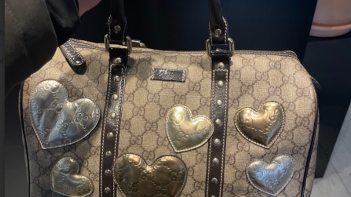 Un sac griffé Gucci avec des cœurs, devant un comptoir rempli de sacs. 