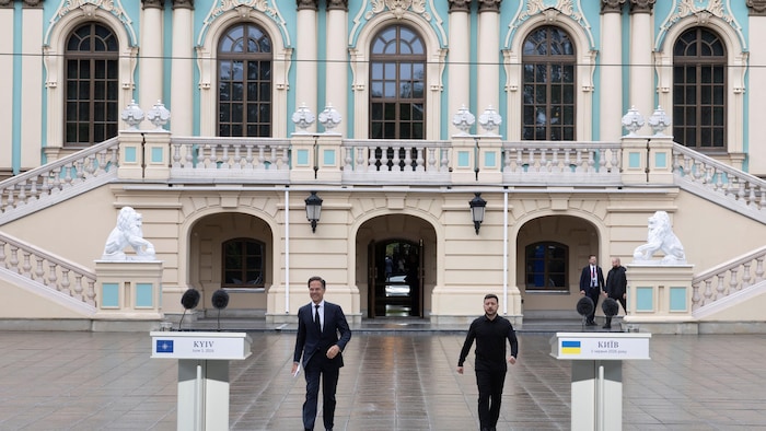 Mark Rutte et Volodymyr Zelensky s'approchent de micros, devant un imposant bâtiment.