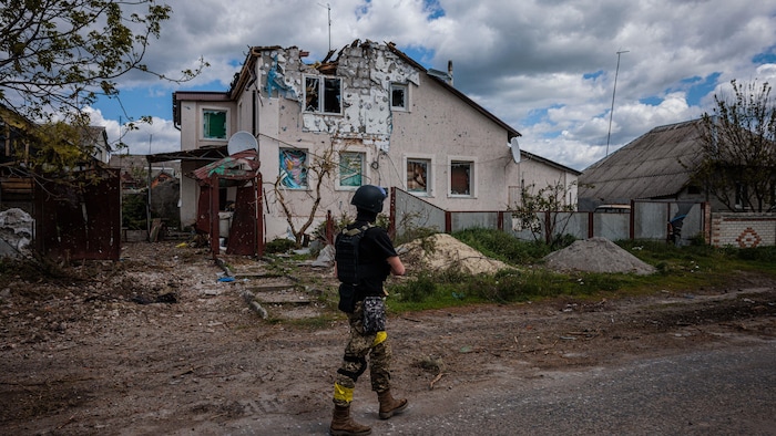 Un soldat ukrainien marche devant une maison bombardée.