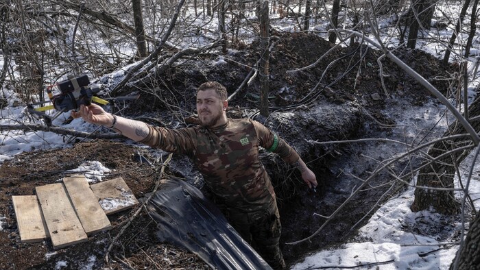 Un soldat se tenant dans un trou dans le sol tend le bras avec lequel il lance un drone.