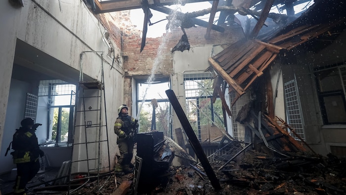 Un pompier à l'intérieur d'un bâtiment en ruines envoie un jet d'eau vers le ciel.