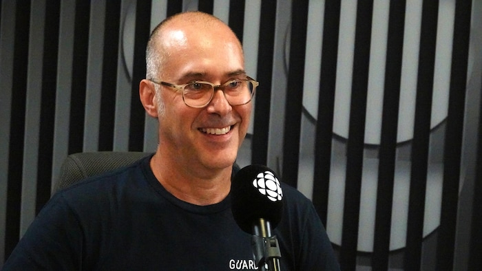 Un homme souriant assis derrière un microphone.