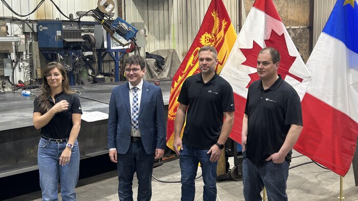 Guillaume Thériault-Deschênes, François Bossé et d'autres représentants de Max Steel dans l'usine devant des drapeaux du Nouveau-Brunswick, du Canada et de l'Acadie.