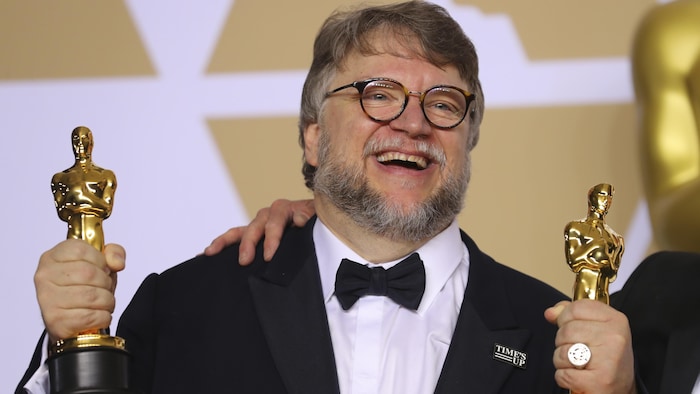 Guillermo del Toro tient un Oscar dans chaque main, tout souriant.