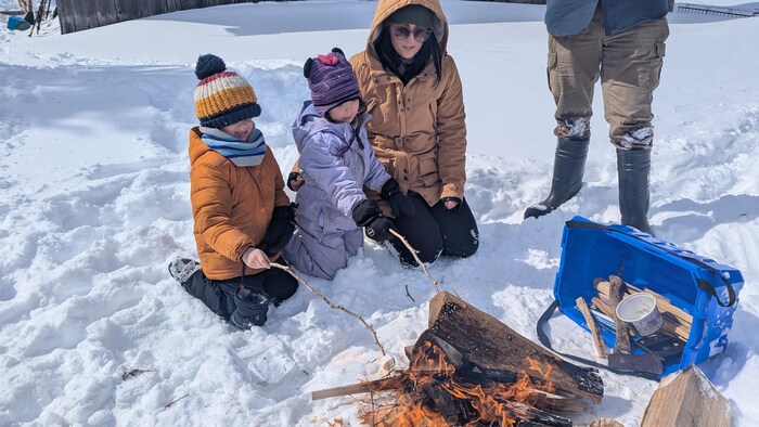 Des enfants font griller des guimauves sur un feu à l'extérieur avec leur enseignante.