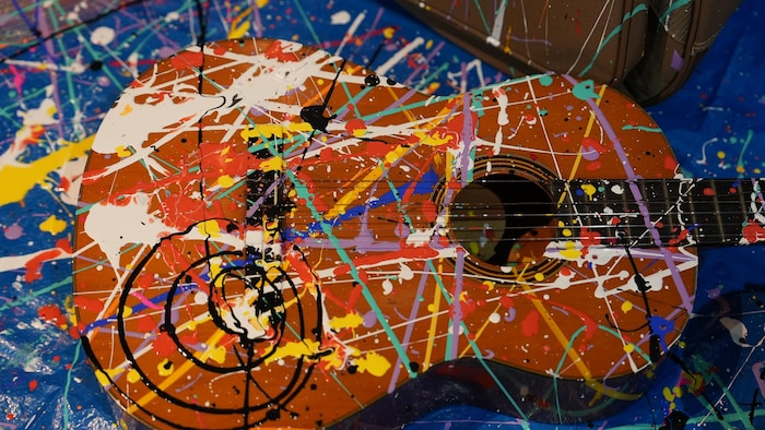 Une guitare marquée de traits de peinture est déposée sur une bâche.