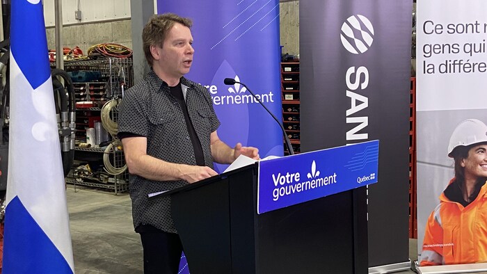 Un homme debout derrière un pupitre parle à son auditoire.  