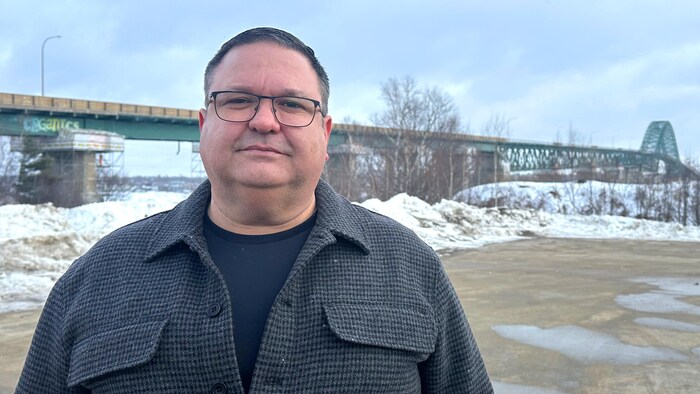 Un homme est debout à l'extérieur devant un pont au loin.