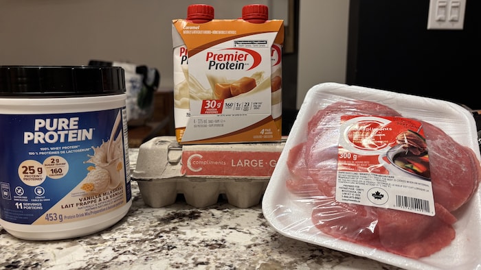 Des aliments protéinés sur un comptoir (poudre protéinée, œufs, viande rouge et boisson protéinée).