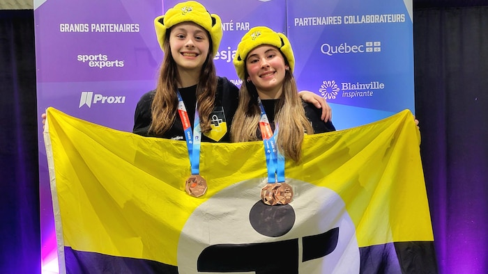 Deux adolescentes ont des médailles de bronze au cou et tiennent un drapeau de la délégation du Centre-du-Québec des Jeux du Québec.