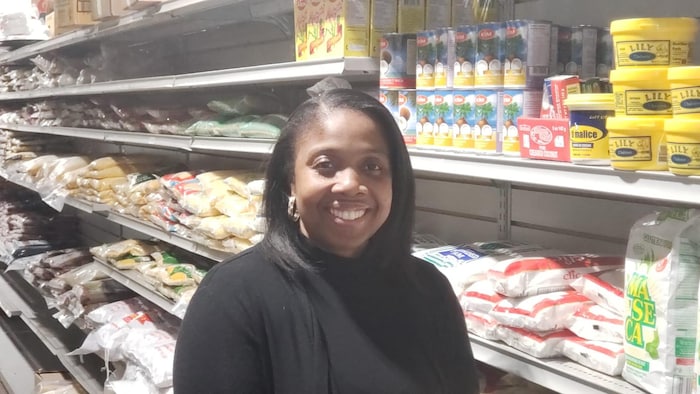 Mirmonde Saint Jean sourit dans l'allée des étagères de son épicerie remplie de produits importés d'Haïti.