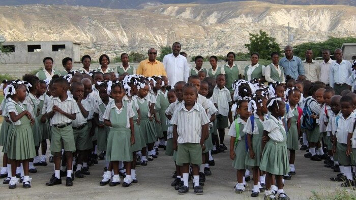Des élèves de l'école élémentaire Saint-Paul, en rang sur le site de l'établissement en construction, accompagnés de M. Antoine Dérose et du corps enseignant. En arrière plan, les montagnes déboisés d'Haïti.