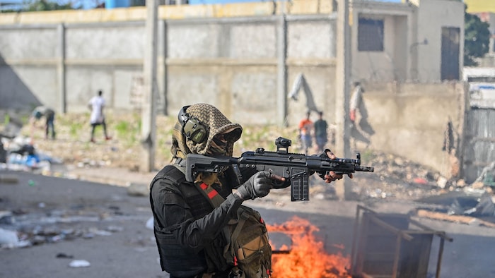 Un policier tient une arme dans une rue dévastée.