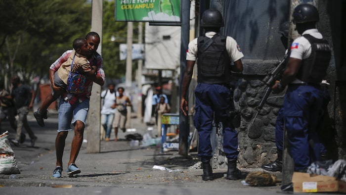 A parent, carrying his child after picking him up from school, runs past police as they carry out an operation against gangs in the Bel-Air area of Port-au-Prince on March 3, 2023. (Odelyn Joseph/The Associated Press )