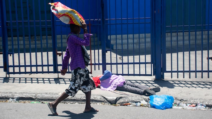 Un passant, sac sur la tête, marche dans la rue et observe un cadavre.