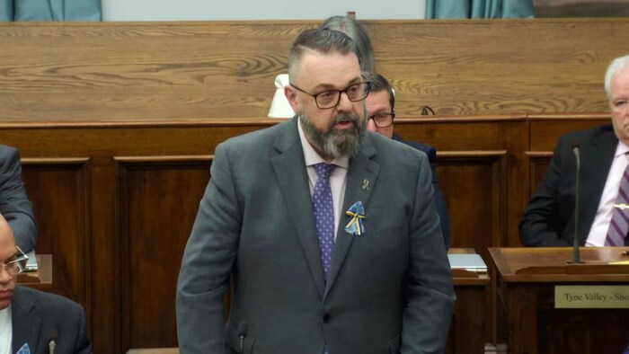 Hal Perry, debout, s'adresse à l'Assemblée législative.