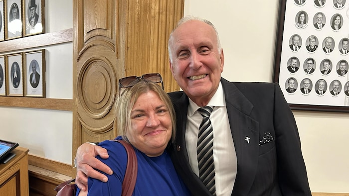 Haley Flaro et Paul Ouellet sourient à la caméra à l'extérieur de la salle de l'Assemblée législative. 