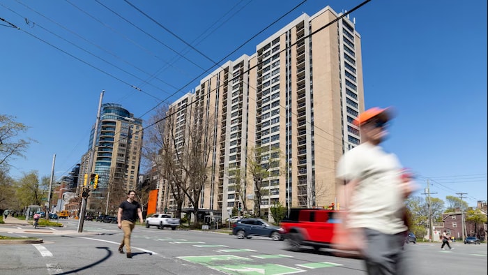 Des passants traversent une rue devant des immeubles résidentiels.