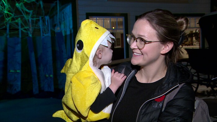 Nicole Casavant répond aux questions de la journaliste Geneviève Patterson au Western Development museum de Saskatoon. Elle sourit et tient dans ses bras sa fille Lina, qui pour l'Halloween, est déguisée en requin. 