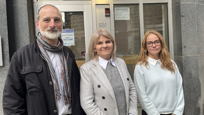 Trois personnes posent en souriant devant la porte d'entrée d'un immeuble.