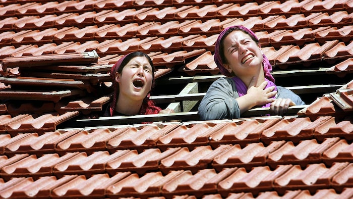 Deux femmes pleurent, la tête sortant d'un trou dans le toit d'une maison.