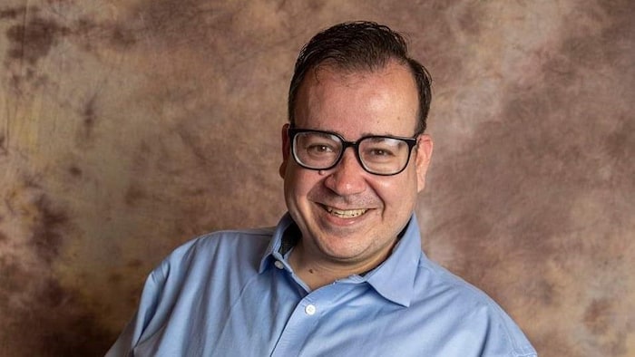 Anthony Frisina est très souriant, il porte une chemise et est assis dans son fauteuil roulant.