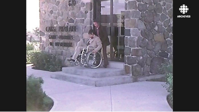 Un homme qui aide un handicapé en fauteuil roulant à monter un escalier.