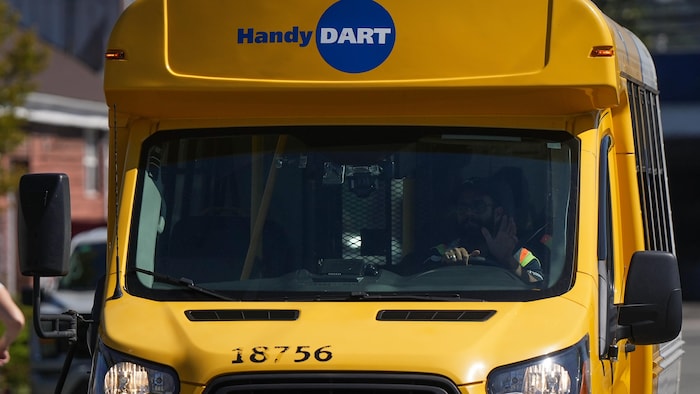 Un bus Handydart. Le chauffeur fait un signe de la main à travers le parebrise.