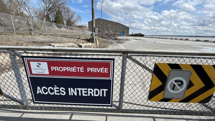 Une affiche qui porte la mention « Propriété privée, accès interdit » est posée sur une clôture en métal devant le hangar numéro 1 au loin.